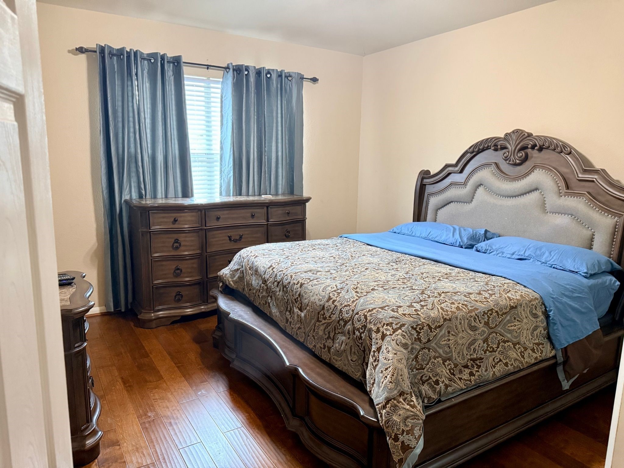 21831 Catoosa Drive Spring, TX 77388 - Photo 9 of 12 This cozy bedroom features warm wooden flooring and a large, ornate bed with matching dresser. The room is softly lit by natural light filtering through elegant curtains, creating a welcoming ambiance.