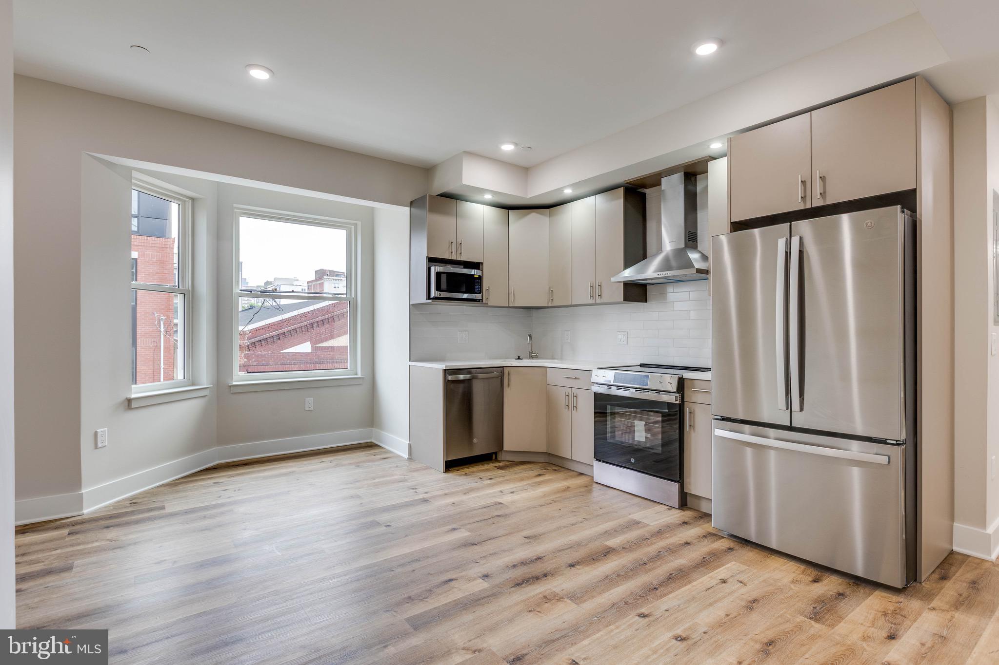 a kitchen with a refrigerator stainless steel appliances wooden floor and window