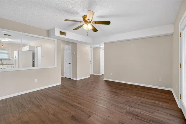 a view of an empty room with wooden floor and a ceiling fan