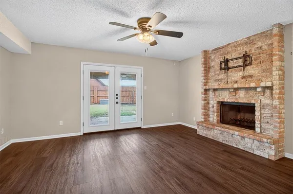 a view of an empty room with wooden floor a fireplace and a window