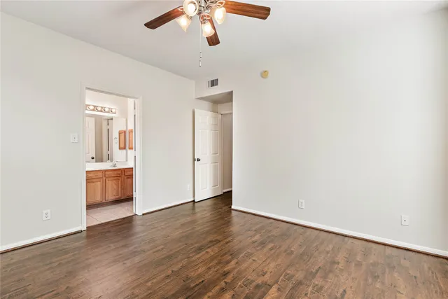 an empty room with wooden floor chandelier fan and windows