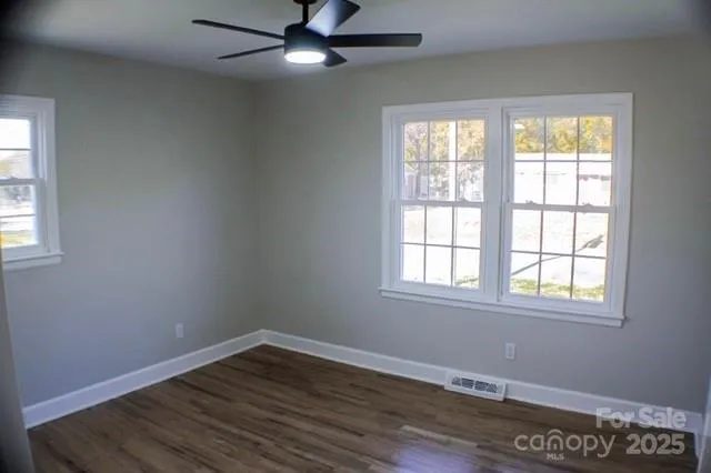 an empty room with wooden floor windows and fan