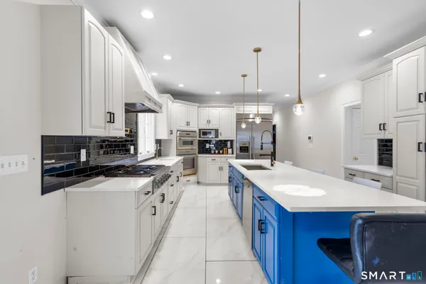 a large white kitchen with stainless steel appliances a sink a stove a refrigerator and a dining table with wooden floor