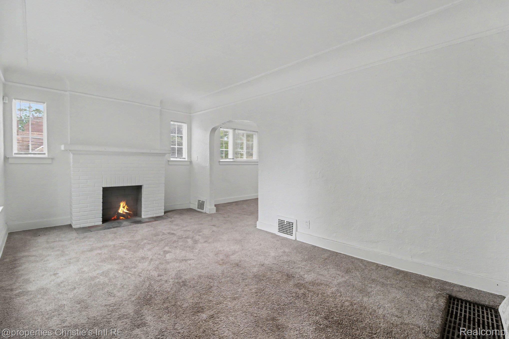 5911 Yorkshire Road Detroit, MI 48224 - Photo 3 of 14 Living area featuring a brick fireplace, arched doorway, multiple windows, textured walls, and carpet flooring