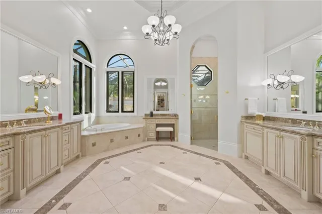 a spacious en suite bathroom with a granite countertop double vanity sink a mirror a bathtub and a window