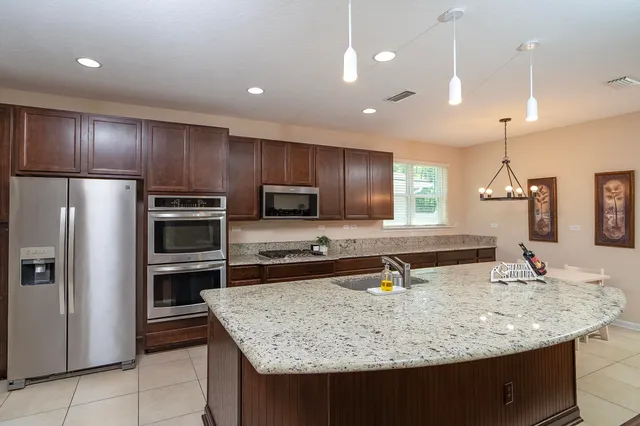a kitchen with kitchen island granite countertop a sink refrigerator and microwave