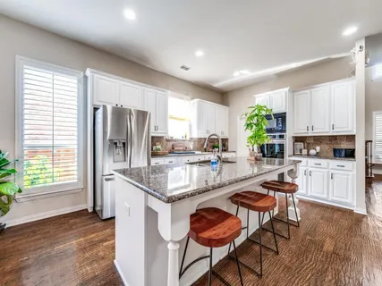 a kitchen with stainless steel appliances kitchen island granite countertop a refrigerator a stove a sink dishwasher and white cabinets with wooden floor