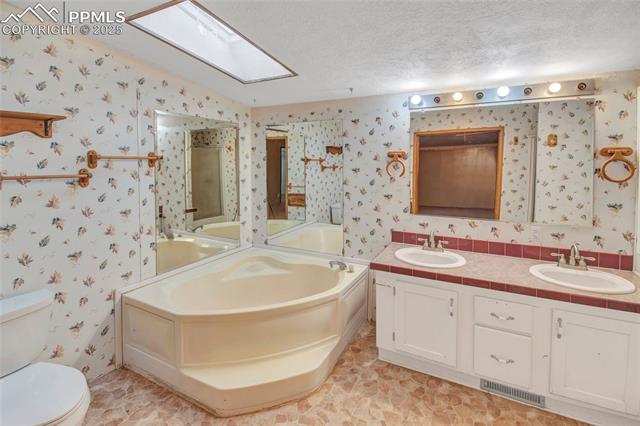 7940 Edison Road Yoder, CO 80864 - Photo 26 of 38 Full bath with a bath, double vanity, a textured ceiling, a skylight, and wallpapered walls