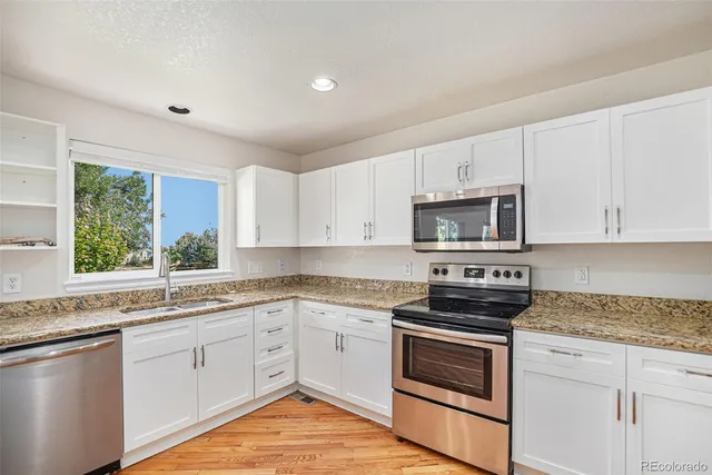 a kitchen with stainless steel appliances granite countertop white cabinets a sink a stove a microwave and wooden floors