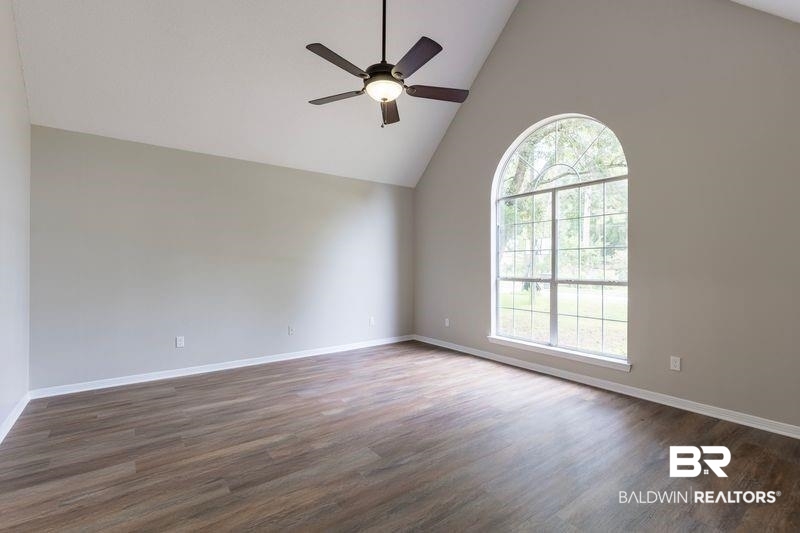 101 Lawson Road Daphne, AL 36526 - Photo 6 of 20 Spacious room featuring a vaulted ceiling with a ceiling fan, a large arched window with grid detailing, wood-finish flooring, and light-toned walls