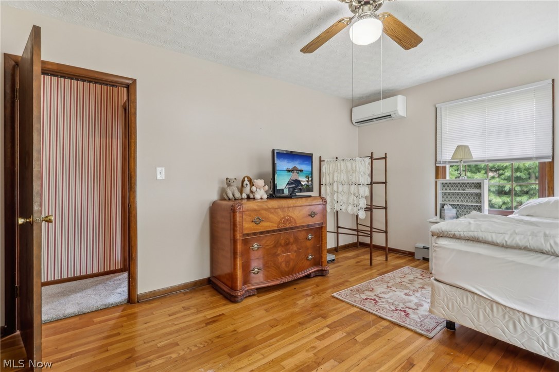 1762 Stonehaven Road Madison, OH 44057 - Photo 19 of 36 Bedroom featuring an AC wall unit, a textured ceiling, ceiling fan, light hardwood / wood-style floors, and a baseboard radiator