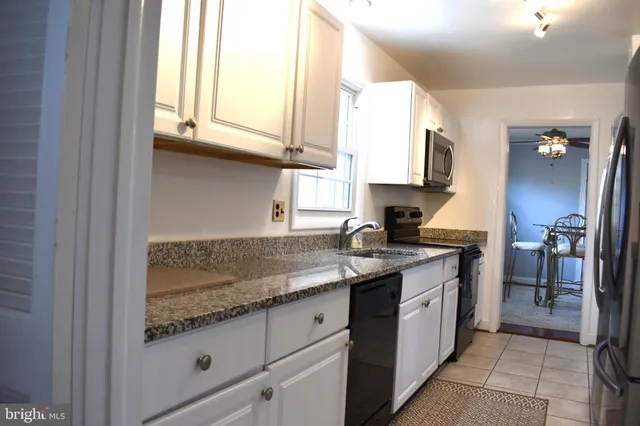 a kitchen with granite countertop a sink stainless steel appliances white cabinets and a window