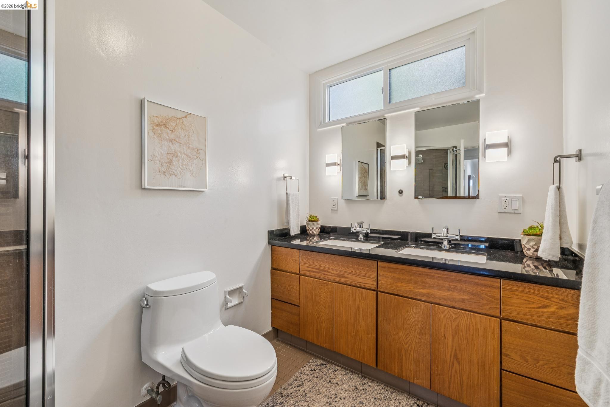 1024 Overlook Road Berkeley, CA 94708 - Photo 31 of 41 Dual vanity with dark stone countertop, wood-finish cabinetry, and contemporary wall-mounted lighting