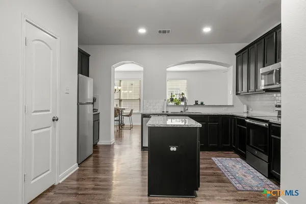 a kitchen with stainless steel appliances granite countertop a refrigerator a sink dishwasher and a oven with wooden floor