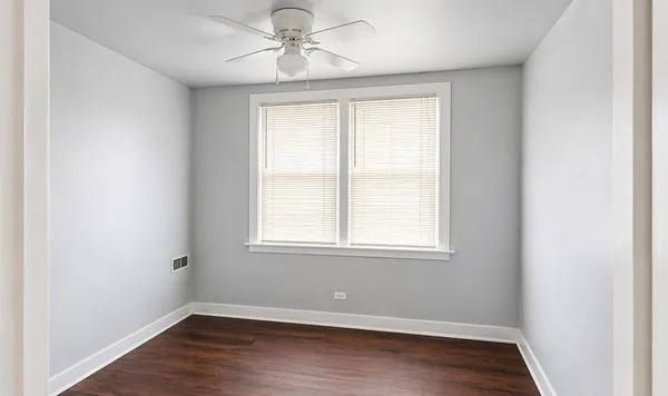 an empty room with wooden floor ceiling fan and window