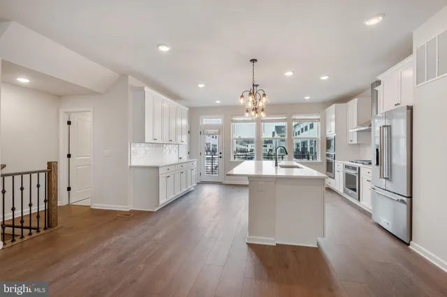 a large kitchen with kitchen island a stove a sink a refrigerator and white cabinets with wooden floor