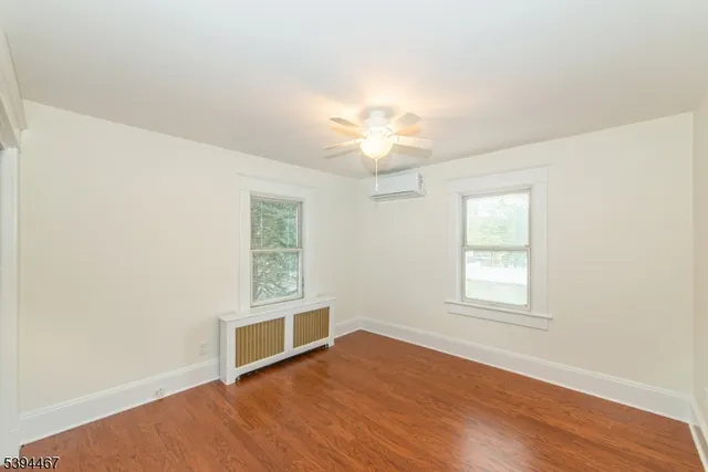 an empty room with wooden floor chandelier fan and windows
