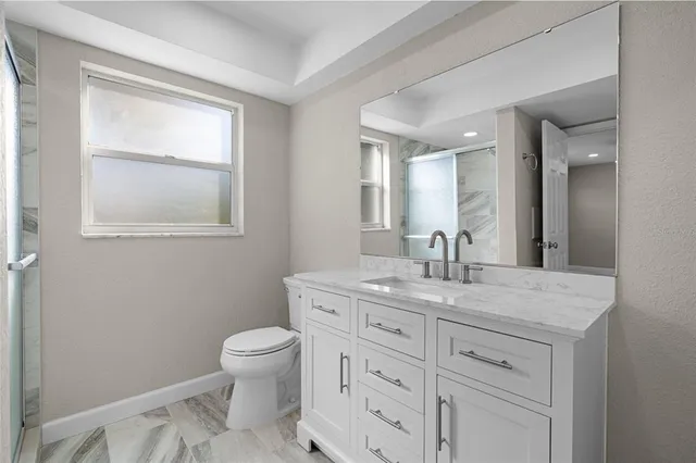 a bathroom with a granite countertop toilet a sink a mirror and a window