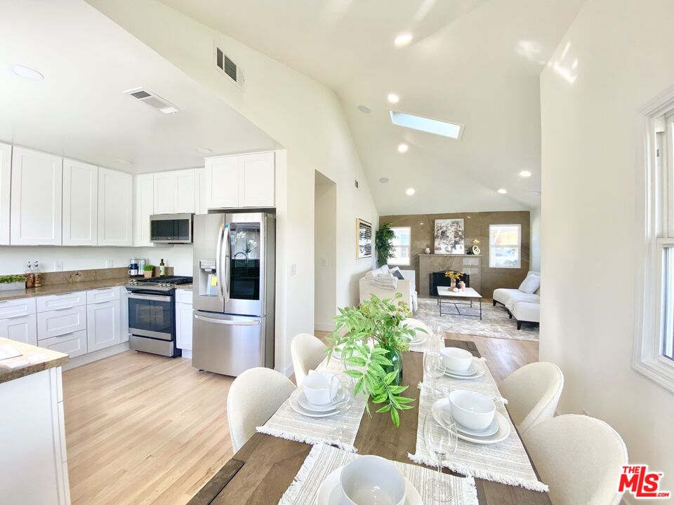 a kitchen with stainless steel appliances kitchen island granite countertop a refrigerator a stove a sink dishwasher a dining table and chairs with wooden floor