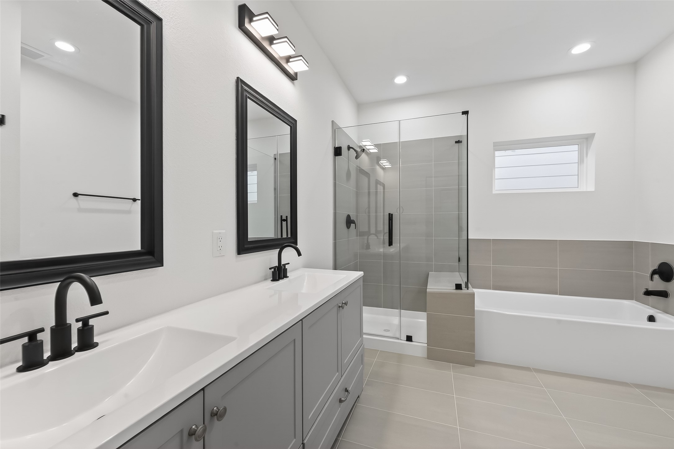3514 Good Hope Street, Unit B Houston, TX 77021 - Photo 22 of 26 This modern bathroom features a dual-sink vanity with sleek black fixtures, a spacious glass-enclosed shower, and a separate bathtub. The neutral tile flooring and walls create a clean and elegant look.