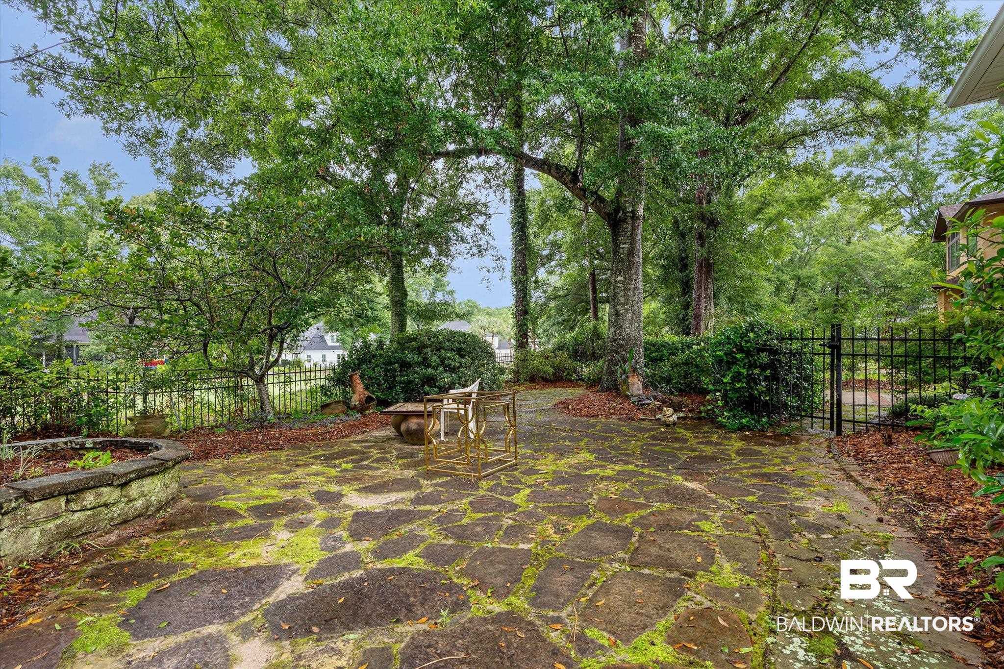 136 Old Mill Road Fairhope, AL 36532 - Photo 30 of 36 Flagstone patio featuring a stone planter, mature trees, and a black wrought iron fence with a gate