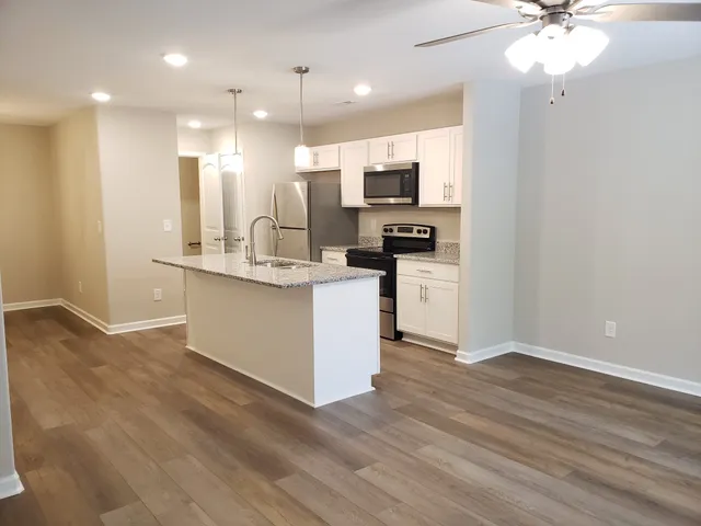 a kitchen with stainless steel appliances kitchen island granite countertop a refrigerator a stove a microwave oven with white cabinets and wooden floor