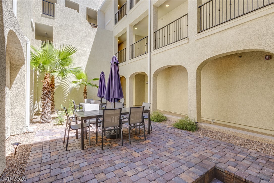 2555 Hampton Road, Unit 8206 Henderson, NV 89052 - Photo 23 of 25 An inviting courtyard features a dining set with umbrellas, surrounded by palm trees and arched architectural details.