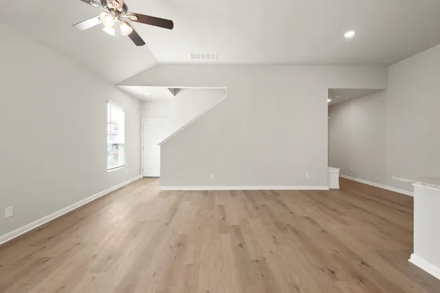 a view of an empty room with wooden floor and a ceiling fan