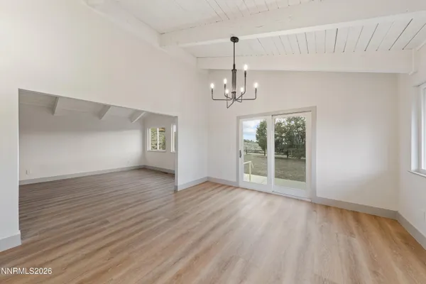 a view of an empty room with wooden floor kitchen view and a window
