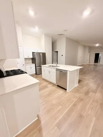 a living room with stainless steel appliances kitchen island hardwood floor and a sink