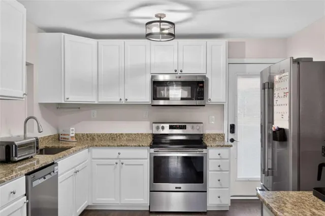 a kitchen with stainless steel appliances granite countertop a refrigerator a stove a sink and white cabinets