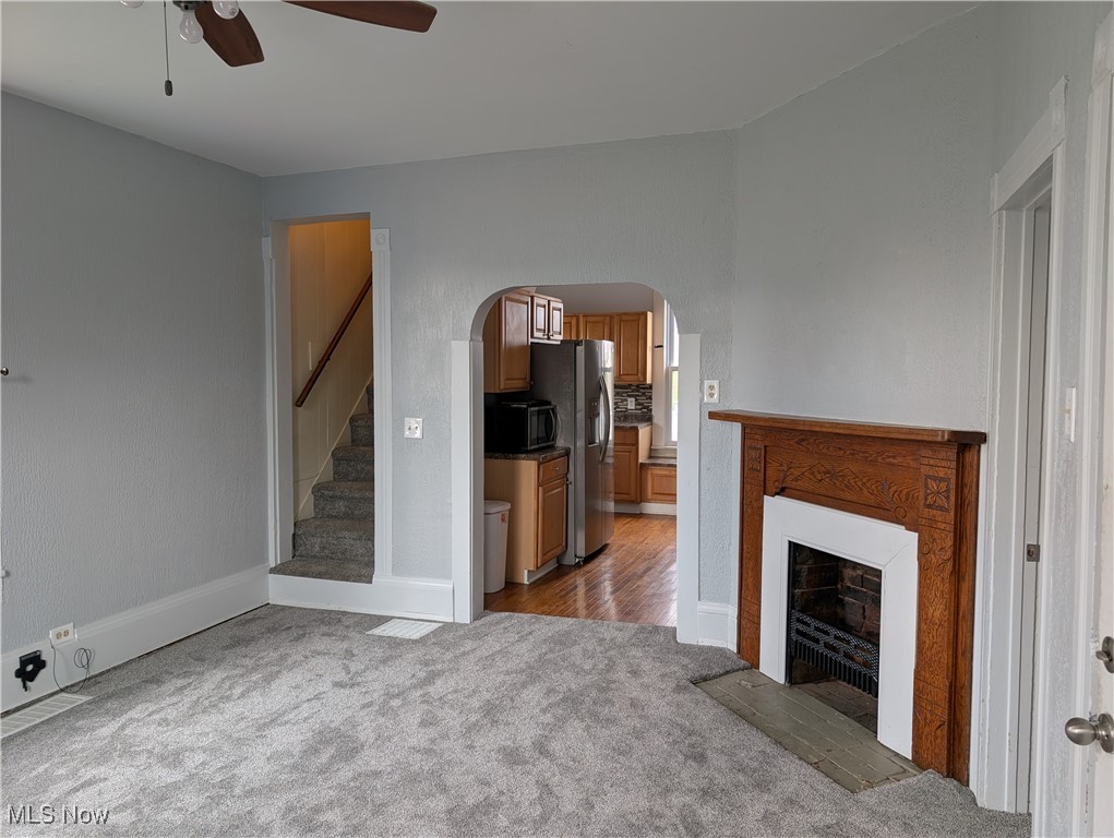 10143 Pleasant Road Pleasant City, OH 43772 - Photo 5 of 32 Living room with a fireplace with flush hearth, dark colored carpet, stairs, ceiling fan, and arched walkways