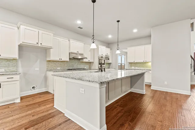 a large kitchen with stainless steel appliances kitchen island granite countertop a sink a stove and a wooden floors