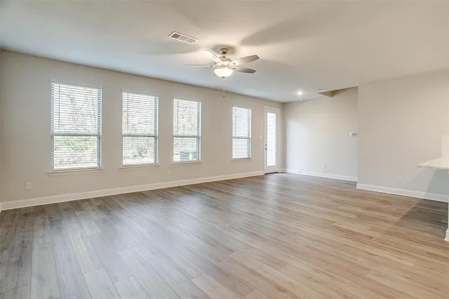 an empty room with wooden floor chandelier fan and windows