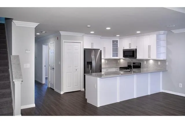 a kitchen with stainless steel appliances granite countertop a refrigerator a sink a stove a microwave and white cabinets with wooden floors