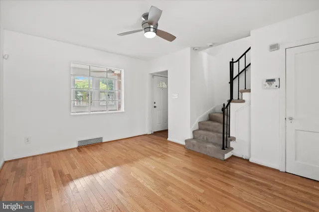 a view of an empty room with wooden floor and a ceiling fan