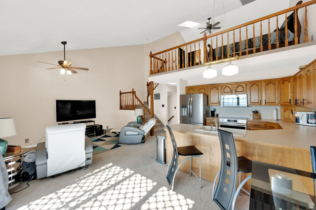 5057 South Ridgedale Drive Ogden, UT 84403 - Photo 27 of 69 Open-concept living area featuring a vaulted ceiling with skylights, an upper-level loft with wood railing, a kitchen with wood cabinetry and stainless steel appliances, and a breakfast bar