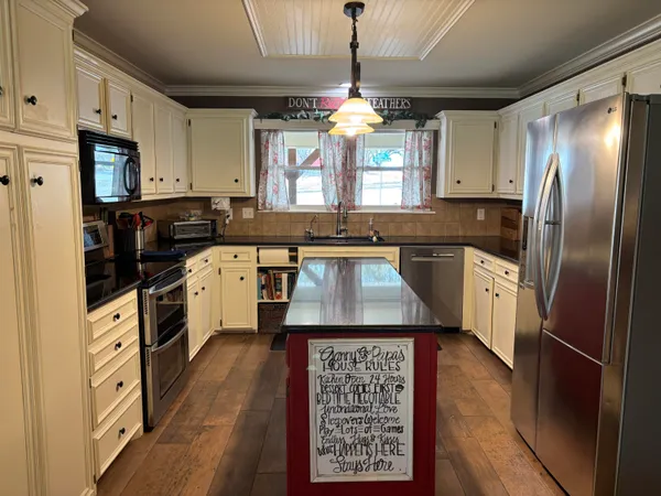 a room with stainless steel appliances kitchen island granite countertop a refrigerator a stove and a dining table with wooden floor