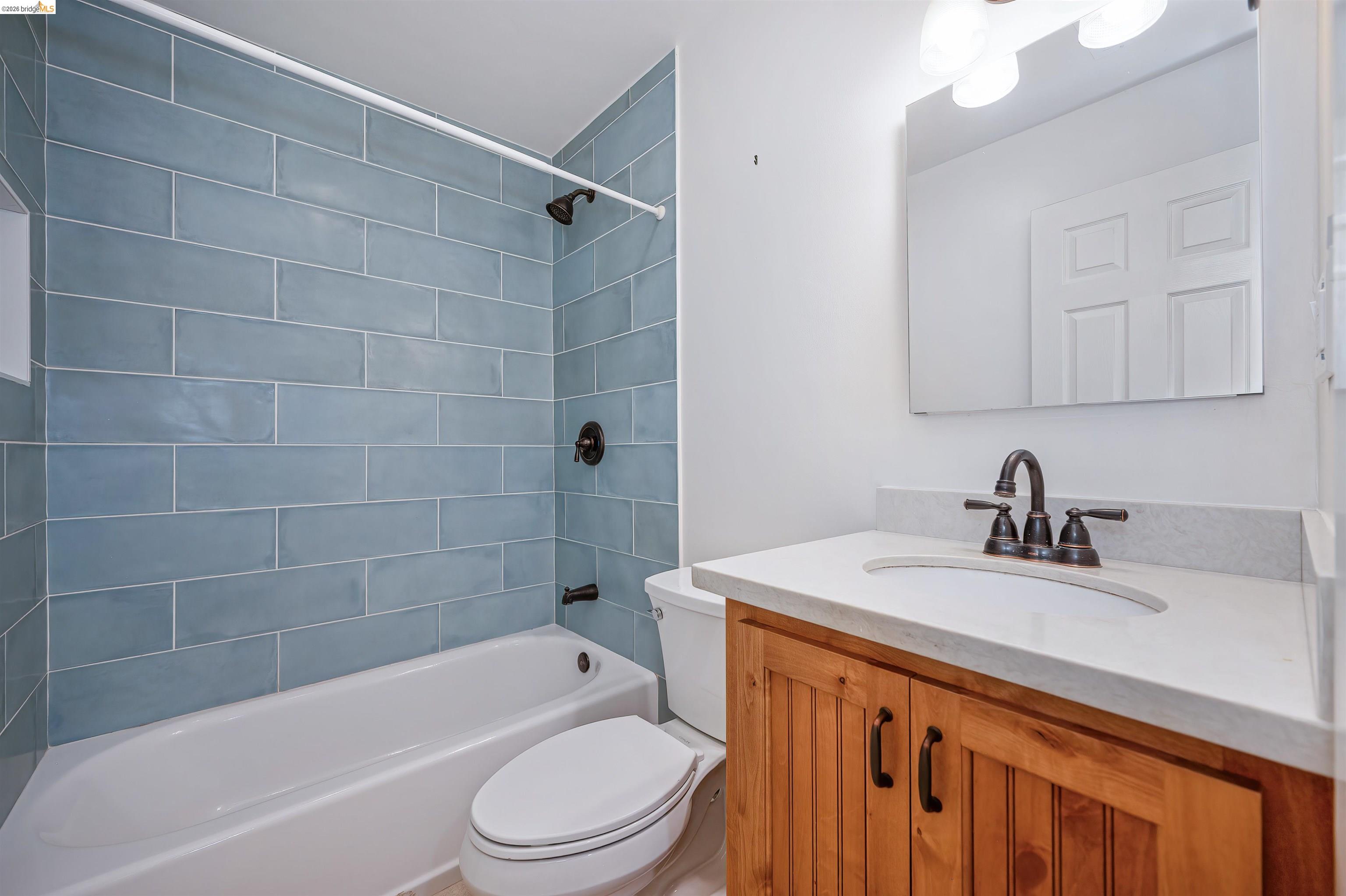 10474 Sheldon Road Elk Grove, CA 95624 - Photo 43 of 83 Bathroom featuring a white bathtub with blue subway tile surround, oil-rubbed bronze fixtures, a vanity with wood-finish cabinetry, a light-colored countertop, and a framed mirror