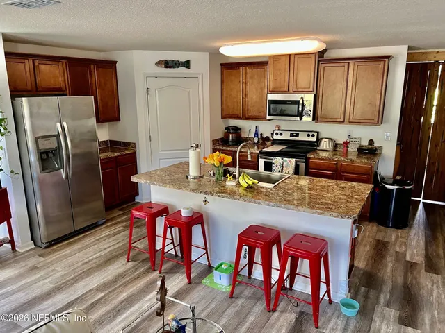 a kitchen with stainless steel appliances granite countertop a refrigerator a stove a sink a dining table and chairs with wooden floor