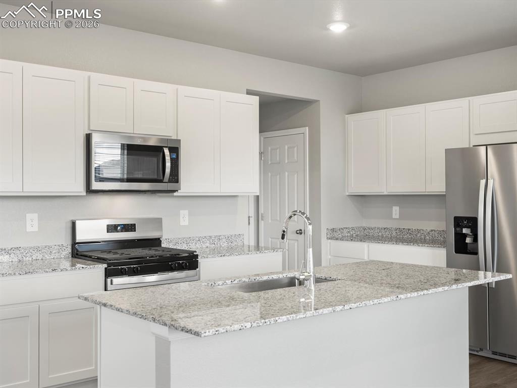 6754 Roundtail Way Colorado Springs, CO 80925 - Photo 8 of 31 a kitchen with granite countertop a sink a stove a microwave and cabinets