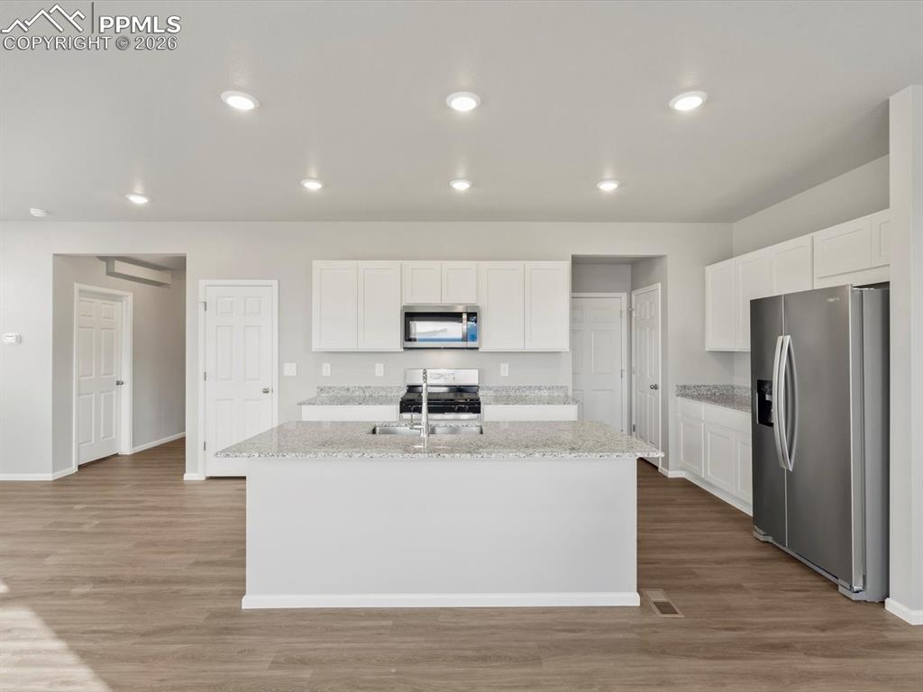6754 Roundtail Way Colorado Springs, CO 80925 - Photo 9 of 31 a large white kitchen with a refrigerator a kitchen island white cabinets and wooden floor