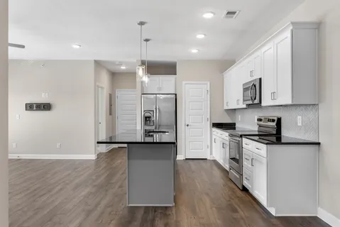 a view of kitchen with stainless steel appliances granite countertop a stove a sink a refrigerator and white cabinets with wooden floor