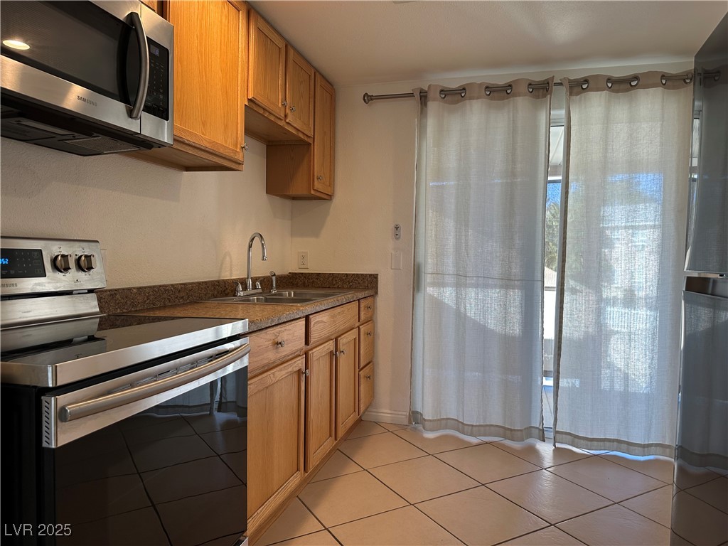 628 B, Unit C Boulder City, NV 89005 - Photo 4 of 12 Kitchen with brown cabinets, a sink, dark countertops, stainless steel appliances, and light tile patterned flooring