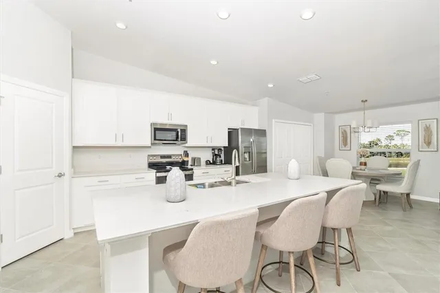 a kitchen with stainless steel appliances kitchen island granite countertop a sink dishwasher a stove a kitchen island with chairs and white cabinets