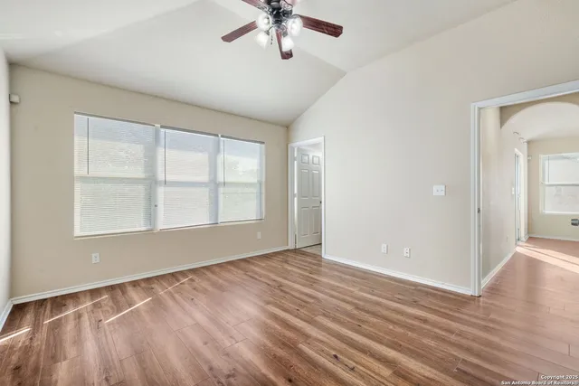 an empty room with wooden floor chandelier fan and windows