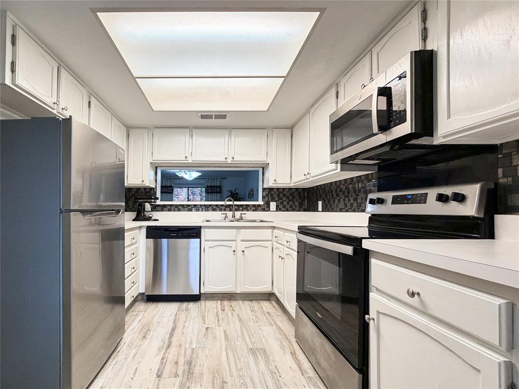 4565 North O'Connor Road, Unit 1304 Irving, TX 75062 - Photo 10 of 32 Kitchen featuring white cabinetry, stainless steel appliances, a dark mosaic tile backsplash, light wood-finish flooring, and a large overhead skylight