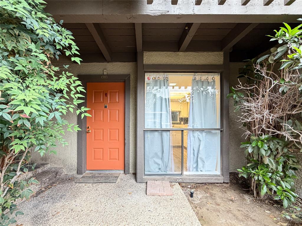 4565 North O'Connor Road, Unit 1304 Irving, TX 75062 - Photo 28 of 32 Exterior entry featuring a vibrant orange door with paneled detailing, an overhead wood trellis, and surrounding mature foliage