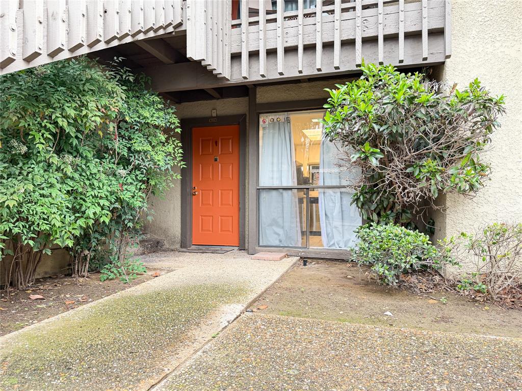 4565 North O'Connor Road, Unit 1304 Irving, TX 75062 - Photo 29 of 32 Entryway featuring a vibrant orange paneled door, large exterior window, and mature shrubbery