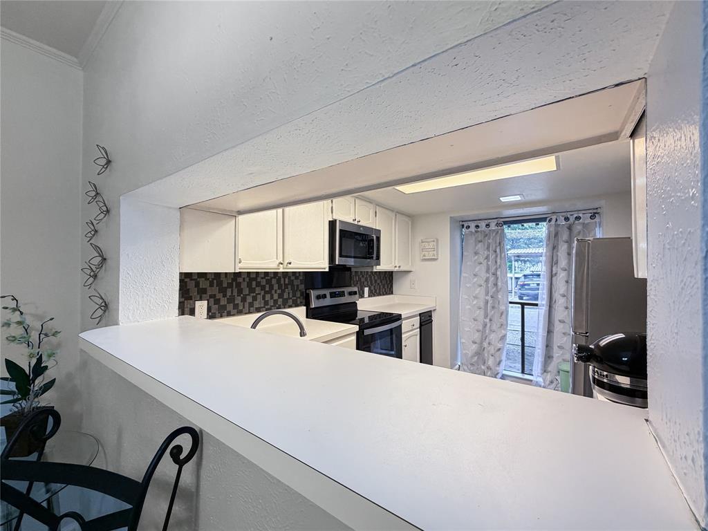 4565 North O'Connor Road, Unit 1304 Irving, TX 75062 - Photo 6 of 32 Kitchen featuring a pass-through window with a breakfast bar, white cabinetry, dark mosaic tile backsplash, and stainless steel appliances